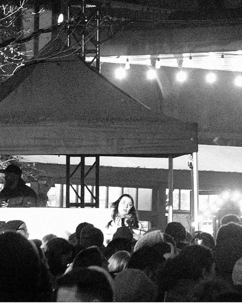Victoria Williston at the microphone on a small stage in front of a crowd at the ByWard Market tree lighting